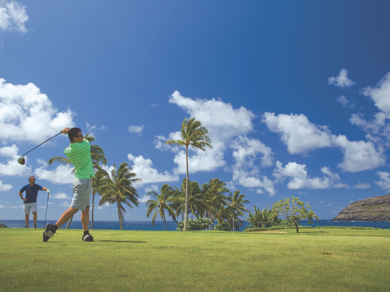Man in green shirt teeing off on tropical island golf course