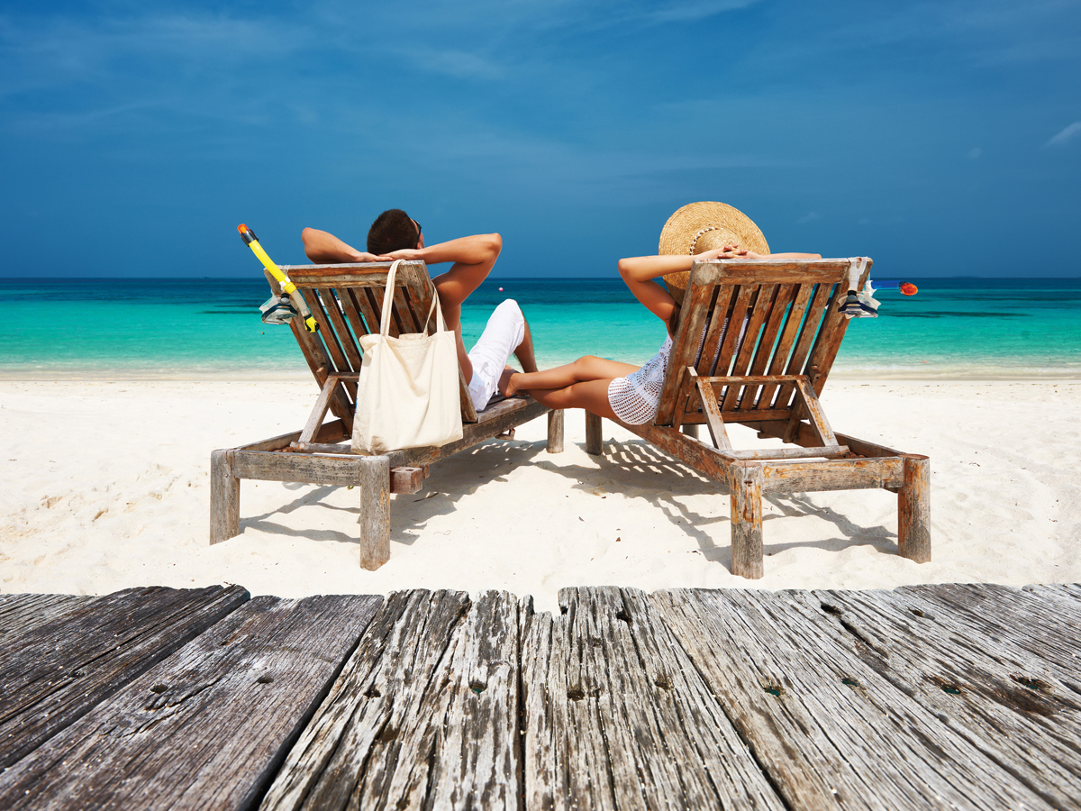 Couple relaxing in wooden beach chairs on white-sand tropical beach