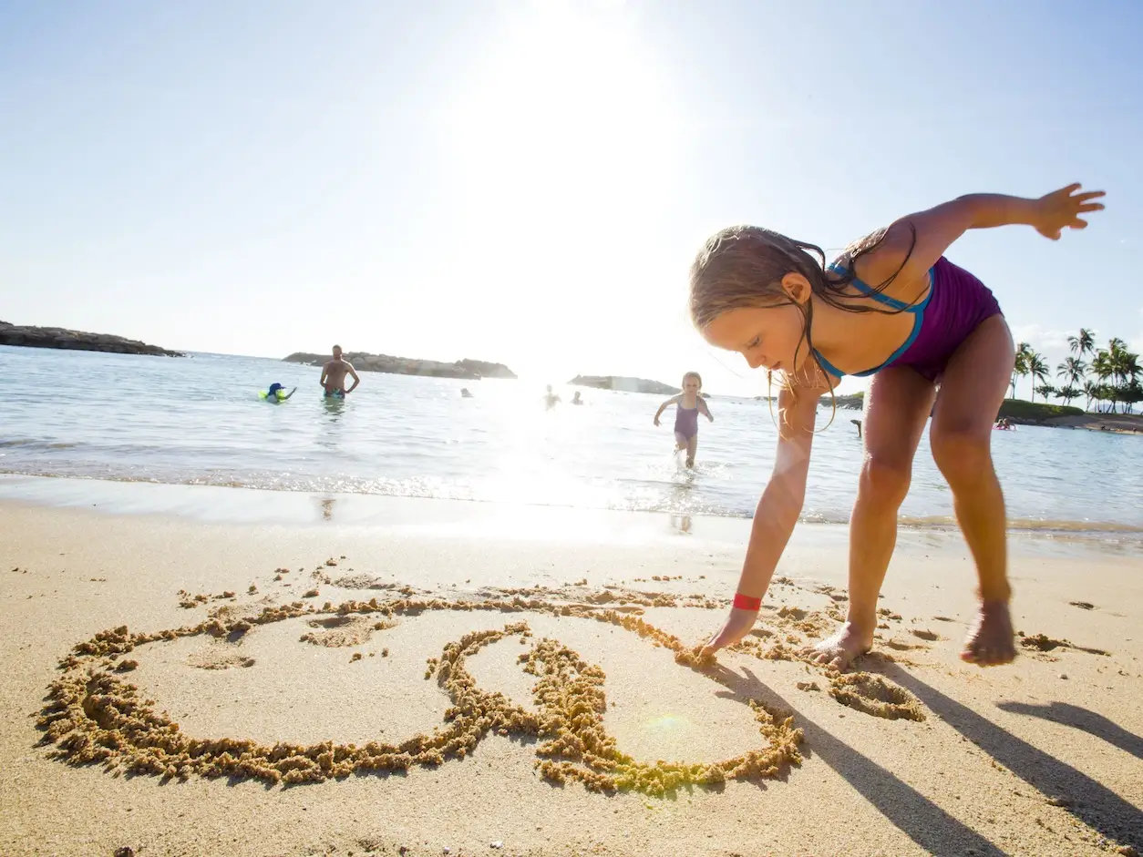 Young girl on sunny beach drawing designs in the sand